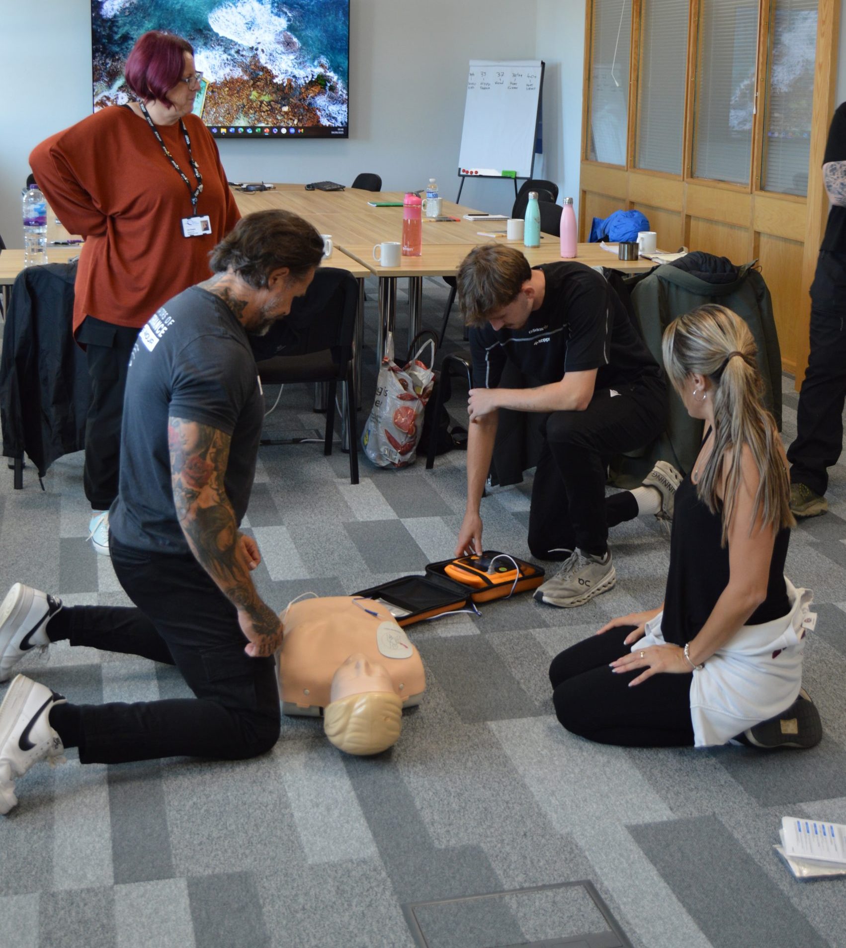 Group demonstrating chest compressions with AED. EFAW Emergency first aid training.