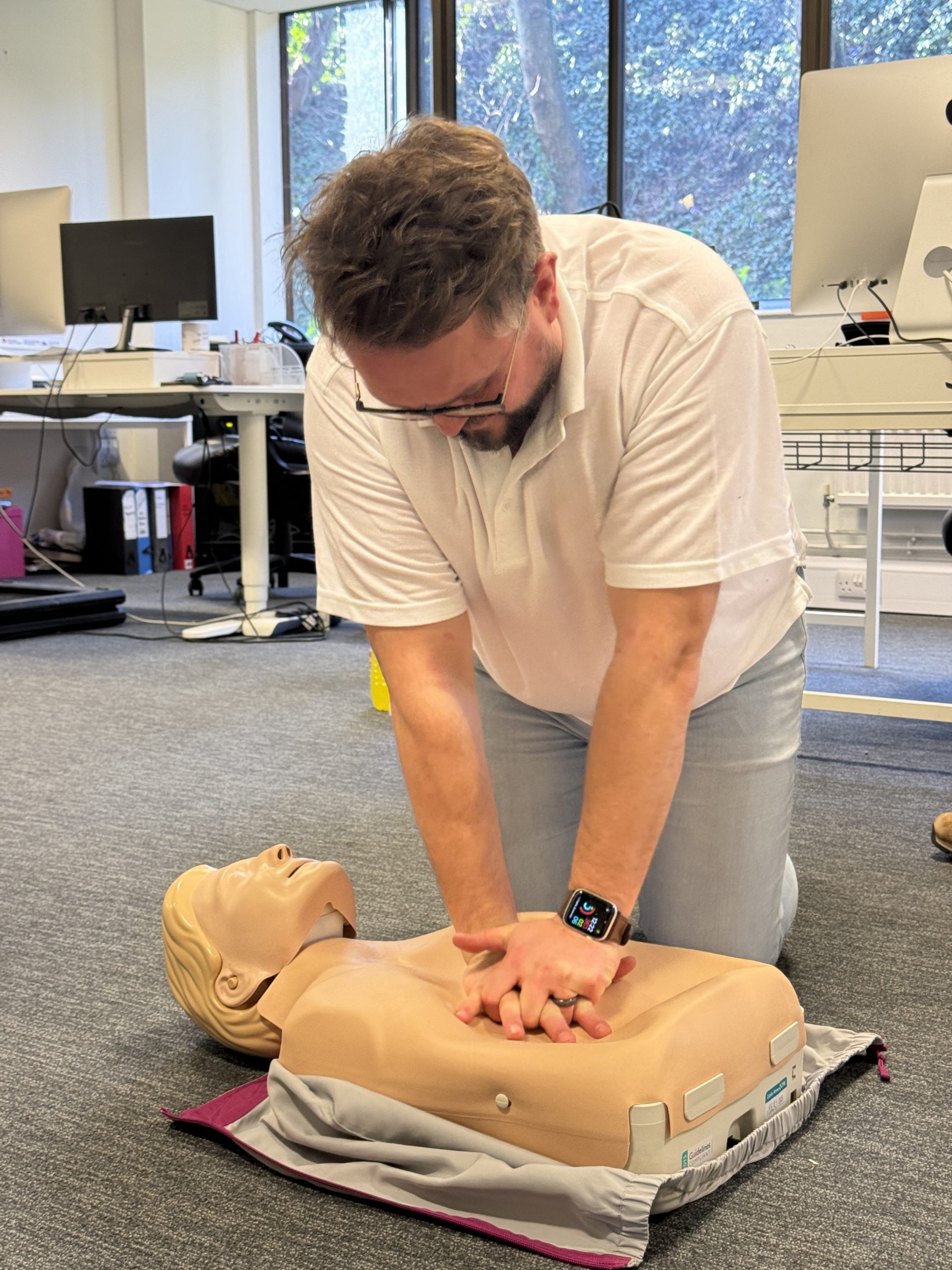 trainer in white top demonstrating chest compressions with AED. EFAW Emergency first aid training.