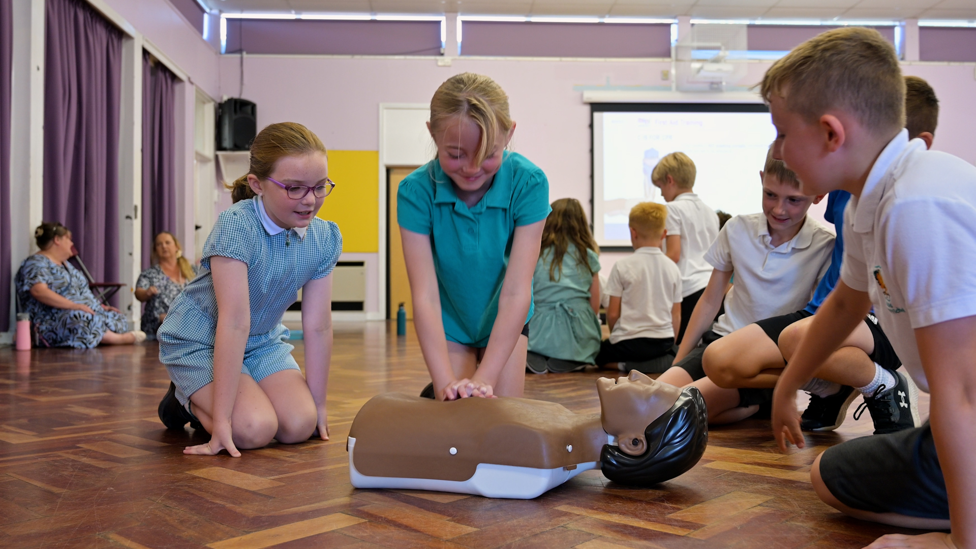 School child in Green top, doing compressions on First Aid Manikin. Mini Medics Training