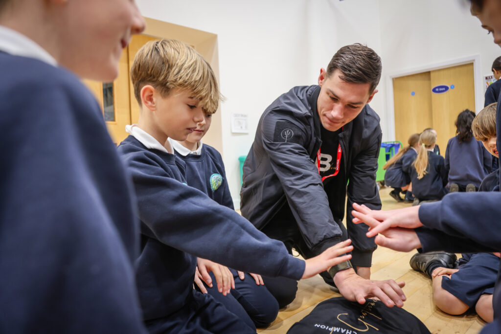 Chris Billam-Smith teaching CPR to 5 pupils who are surrounding the manikin.