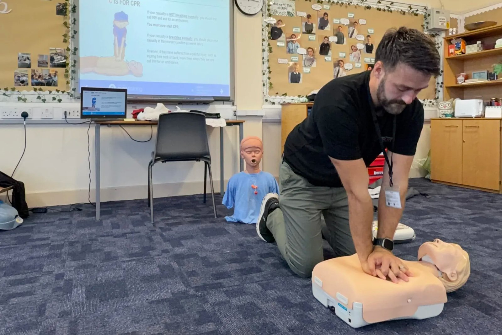 Trainer demonstrating CPR on a manikin in a primary school classroom